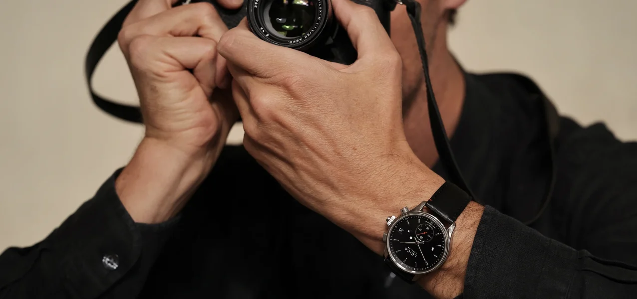 Die Leica Camera ZM 2 Uhr mit Handaufzug am Handgelenk zusammen mit einer Kamera, dritte Ansicht.