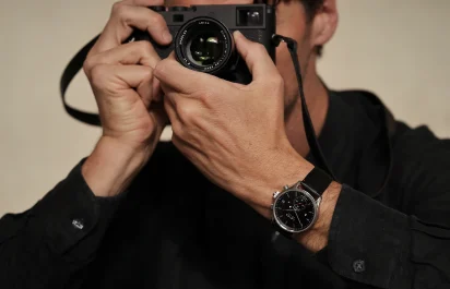 Die Leica Camera ZM 2 Uhr mit Handaufzug am Handgelenk zusammen mit einer Kamera, dritte Ansicht.