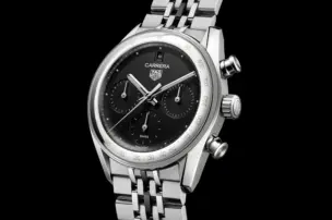 Die TAG Heuer Carrera Chronograph mit schwarzem Zifferblatt, drei Totalisatoren und silbernem Edelstahlgehäuse am mehrgliedrigen Stahlarmband vor schwarzem Hintergrund in Frontalansicht.