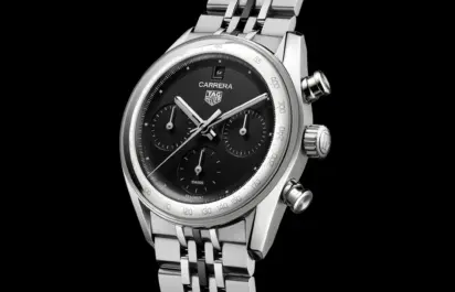 Die TAG Heuer Carrera Chronograph mit schwarzem Zifferblatt, drei Totalisatoren und silbernem Edelstahlgehäuse am mehrgliedrigen Stahlarmband vor schwarzem Hintergrund in Frontalansicht.