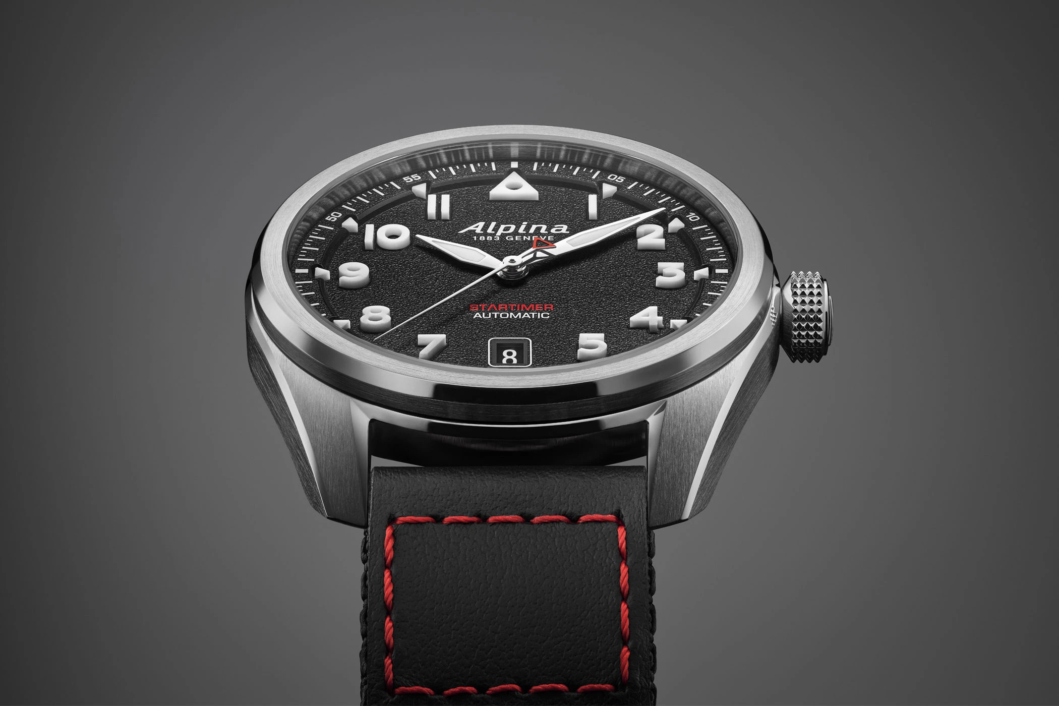 Großaufnahme des Zifferblatts der Startimer Pilot Automatic von Alpina mit schwarzem Zifferblatt und schwarzem Cordura-Band vor grauem Hintergrund.